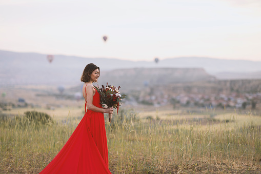 Woman in red dress, sunrise and hot air balloon in Cappadocia.