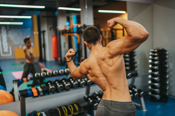 młody muskularny mężczyzna patrzy na siebie w lustrze w krytej siłowni - human muscle back muscular build men zdjęcia i obrazy z banku zdjęć