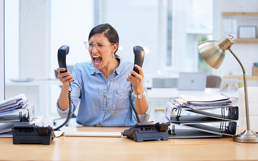 Shot of a young businesswoman screaming in frustration at her telephone