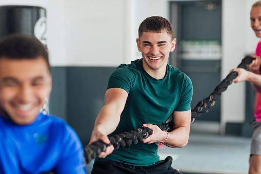 A point of view shot of a small multi ethnic group of young men pulling on a rope at their local gym. They are wearing sports clothing and training in an indoor gym.