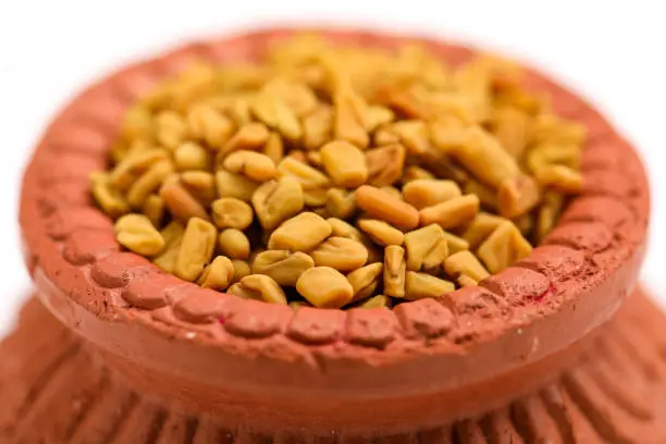 Dry seeds of fenugreek in a clay bowl isolated on white background.