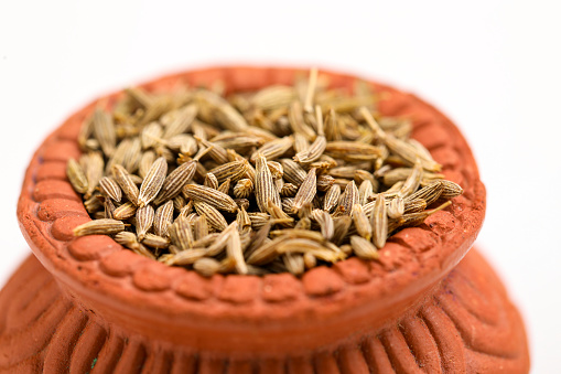 cumin seed in clay bowl on white background.