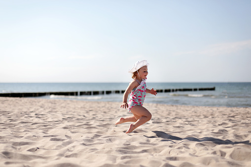 Adorable happy smiling little girl on beach vacation, jumping at the beach