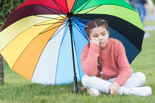 Autumn depression. Spring style. depressive mood in autumn rainy weather. Little girl tired under colorful umbrella. Multicolored umbrella for little happy girl. Rainbow after rain. feeling depressed.