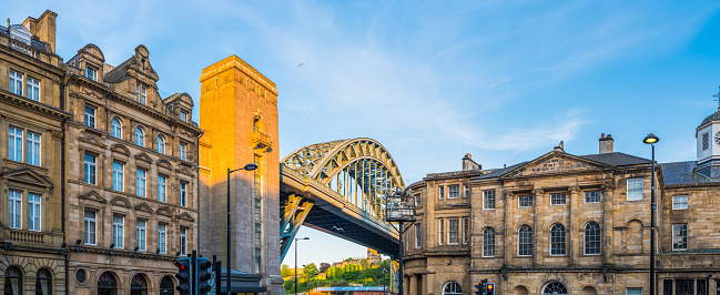 The iconic arch and stone towers of the Tyne Bridge illuminated at sunset above the historic Victorian architecture of central Newcastle, UK.