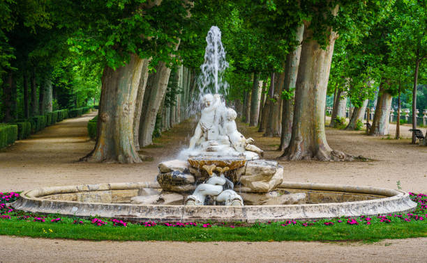 Aranjuez, Spain - June 5, 2021:\n Fountain with water in a public park with large trees in the background. Madrid