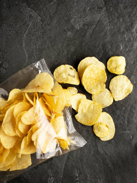 istock Chips spilling out of an open bag, Potato chips package, Potato chips, Chips on Black Background, Chips 1323482974