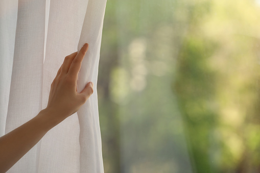 Woman opening white window curtains in room, closeup. Space for text
