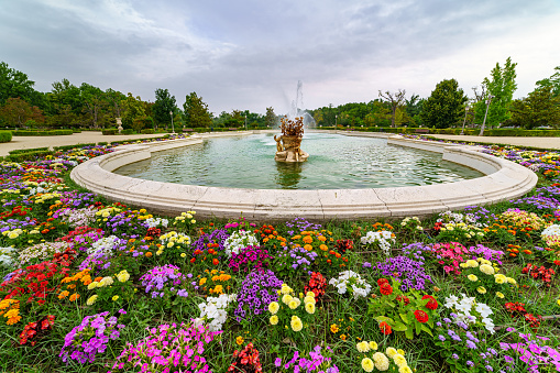 Aranjuez, Spain - June 5, 2021:\n Large fountain in the gardens of the royal palace of Aranjuez with flowers of many colors. Madrid Spain.
