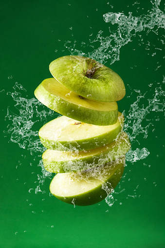Sliced green apple cut splashing water on green background