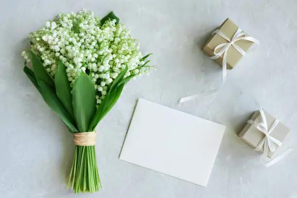 Photo of Greeting card mockup. Bouquet of lilies of the valley, postcard, gift boxes on a light blue background.