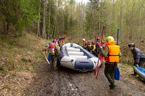 Group of tourists are carrying the rubber raft along the shore to the descent place along the river. Russia, Karelia, Shuja river