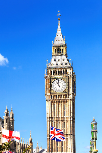 Big Ben with flag of England and United Kingdom in London against blue sky.