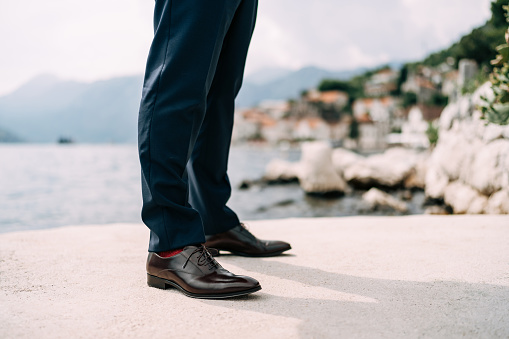 Legs of a man in blue pants, red socks and brown shoes standing on the pier, close-up. High quality photo