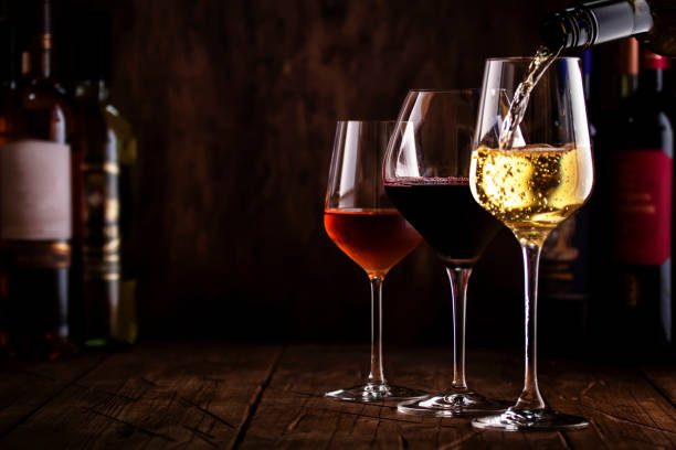 degustazione. vino whte che versa in vetro sullo sfondo con selezione di vini rossi, bianchi e rosati in bicchieri e bottiglie - burgundy foto e immagini stock