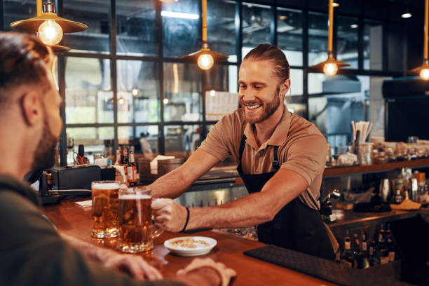 affascinante giovane barista in grembiule che serve birra e sorride - beer bar counter bar drink foto e immagini stock