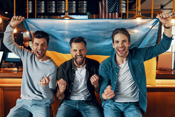 istock Cheering young men covered in Ukrainian flag smiling and looking at camera 1323496777