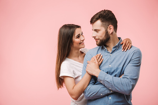 Portrait of a loving young couple hugging while standing isolated over pink background
