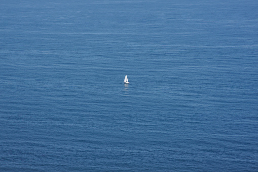 Lonely white sailing boat in the middle of a calm sea. The whiteness of the ship contrasts with the blue of the sea. Copy space. Horizontal photography.