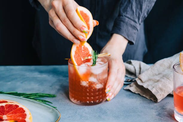 Female bartender hand squeezes juice from fresh grapefruitÂ in cocktail lemonade with ice and rosemary. stock photo