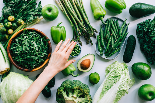 Many market fresh vegetables lined up next to each other in the vibrant colors of a rainbow. Vegetables include; zucchini, broccoli, aubergine, sweet potato radish, red onion, tomato, chili pepper, carrot, bell pepper, onion, garlic, celery, beans and a lemon. Shot from directly above.