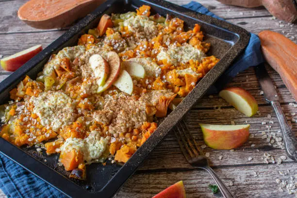 Fitness breakfast casserole with sweet potatoes and apples topped with low fat cottage cheese and cinnamon served hot on a rustic table background. Guten free and clean eating meal