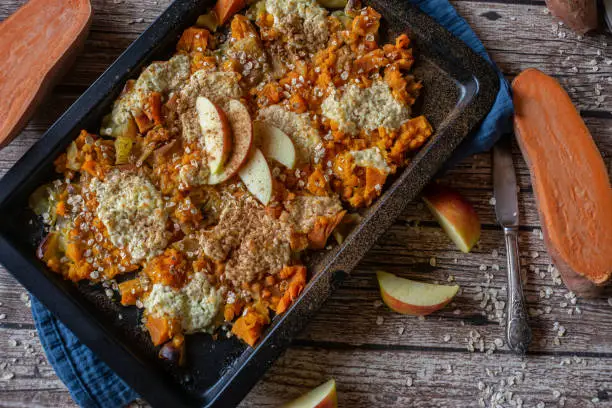 Sweet breakfast casserole with sweet potatoes and apples topped with cottage cheese and cinnamon and served on a baking sheet on rustic table background. Overhead view