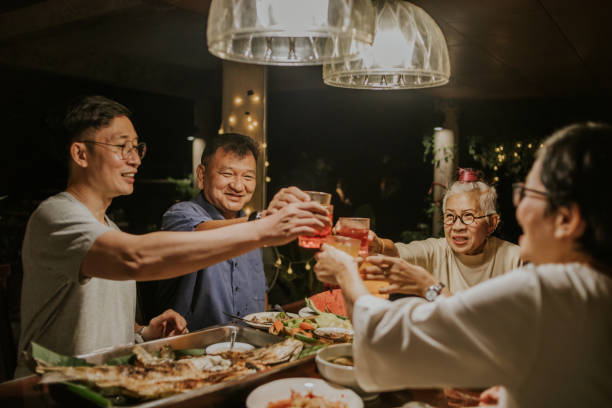 Cheers! Thai family clink while having dinner party-stock photo Thai large family enjoy celebration grandmother's birtday in the evening at home with positive emotion family reunion celebration stock pictures, royalty-free photos & images