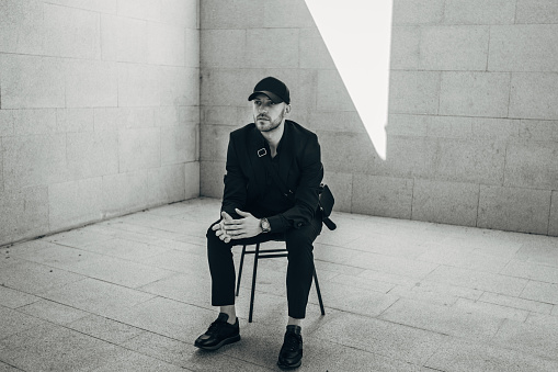 One man, handsome fashionable man sitting on chair by a gray wall..