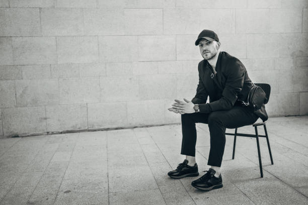 One man, handsome fashionable man sitting on chair by a gray wall..