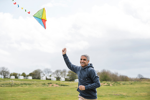 Man flying a kite in a field smiling while looking at the camera in the North East of England.