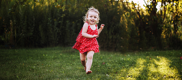 happy baby smiling. a little girl running in the garden at sunset outdoor barefoot. banner