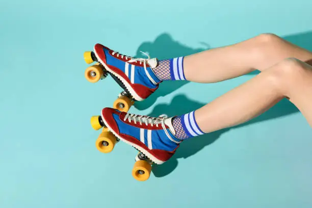 Young woman with thin skinny legs wearing colorful roller skates with yellow wheels and a view of her legs extending from the right over a blue background with copyspace