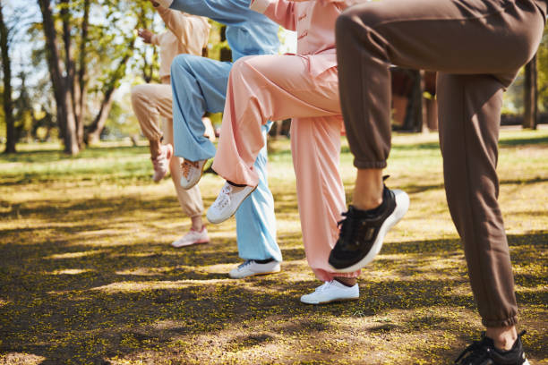 Raised legs of four people, doing exercise in park Group of wushu students lifting their left feet off the ground and standing on one leg during martial arts activity woman legs open stock pictures, royalty-free photos & images