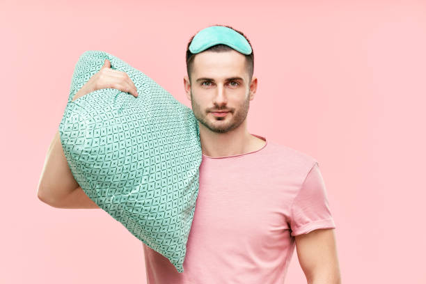 istock Young handsome man in sleeping mask holding pillow in hands 1323511540
