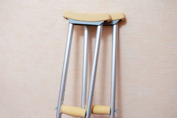 Photo of Medical Concepts. Pair of Crutches for Disabled People Placed Against Wall Indoors.Horizontal Orientation