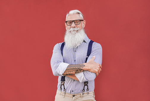 Happy hipster senior man looking in camera and smiling - Trendy elderly person with grey hair and tattoo