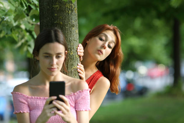 Woman using phone being spied by her friend Woman using phone being spied by her friend stalker stock pictures, royalty-free photos & images