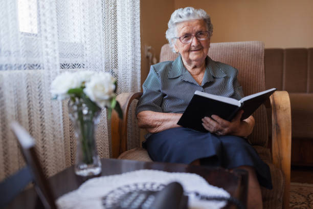 istock Old woman reading a book at home 1323518912
