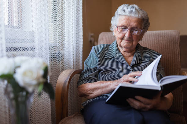 istock Old woman reading a book at home 1323518932