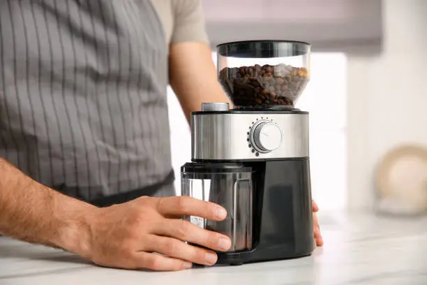 Photo of Man using electric coffee grinder in kitchen, closeup