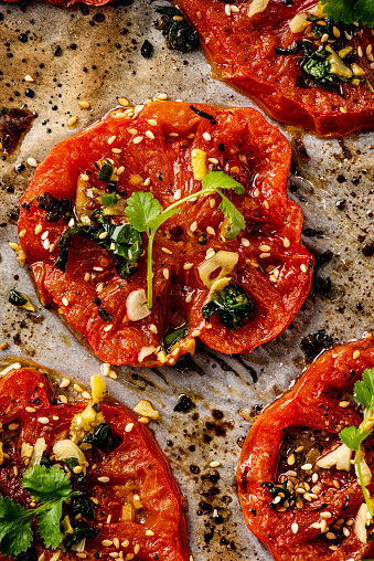 A vegetarian summer dish recipe inspired by Yottam Ottolenghi. Grilled beefsteak tomatoes with; olive oil, green chilli, coriander, garlic and sesame seeds. Cut into thick slices and grilled for around 15 minutes. Colour, vertical format with some copy space.
