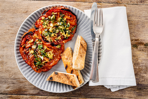 Overhead view of two slices of grilled beefsteak tomato  cooked with; garlic, ginger, coriander and served with sesame seeds. Horizontal format, with some copy space photographed against a rustic wooden background.