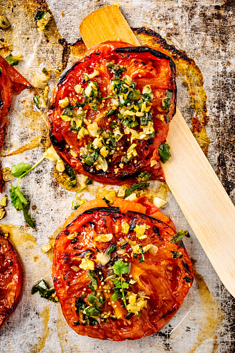 Overhead view of two thick slices of beefsteak or heirloom tomatoes cooked with; garlic, ginger, coriander and sesame seeds. Vertical format, with some copy space photographed on a baking tray just out of the oven.