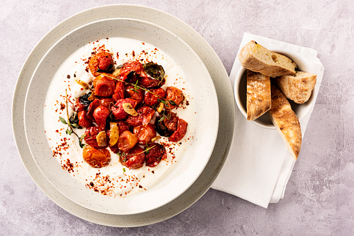 A vegetarian summer salad dish inspired by Yottam Ottolenghi. Oven baked cherry tomatoes with; cumin, garlic, thyme, chilli flakes, fresh oregano, lemon and lemon peel  and some organic brown sugar. Baked for 20 minutes and served with greek yoghurt with lemon and salt and chilli flakes. Colour, horizontal format with some copy space.