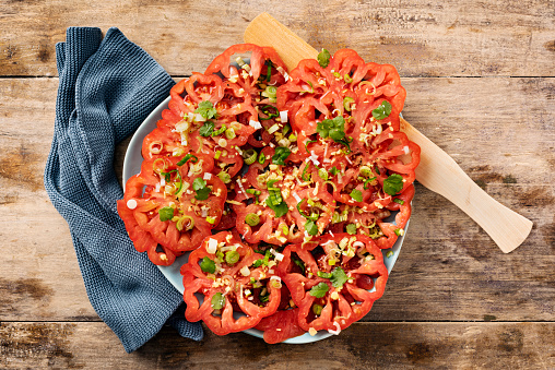 Overhead view of a tomato salad made with heirloom tomatoes thinly sliced with an olive oil dressing made with; ginger, spring onions, chilli, coriander and sherry vinegar. Horizontal format with some copy space.