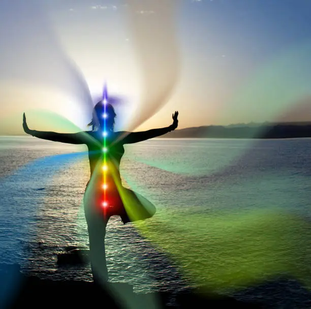 woman in yoga pose on beach sunset view, glowing seven all chakra. Kundalini energy. girl practicing meditation outdoors. Silhouette.