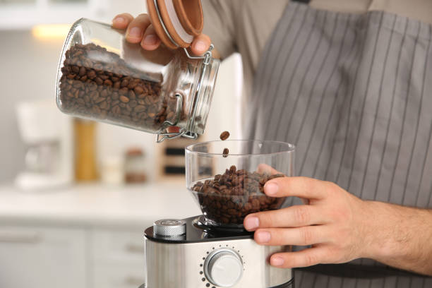 Man using electric coffee grinder in kitchen, closeup Man using electric coffee grinder in kitchen, closeup coffee grinder stock pictures, royalty-free photos & images