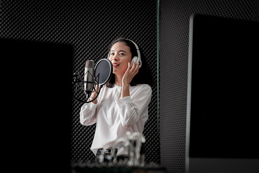 Asian female singer with a passion for music and microphone. While playing her guitar in a professional studio. Music concept, sound recording concept.