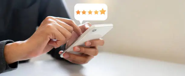 close up on customer man hand pressing on smartphone screen with  five star rating feedback icon and press level good rank for giving best score point to review the service , technology business concept